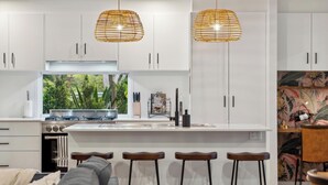 Una cocina moderna con armarios blancos, una isla central con taburetes altos y dos lámparas colgantes.