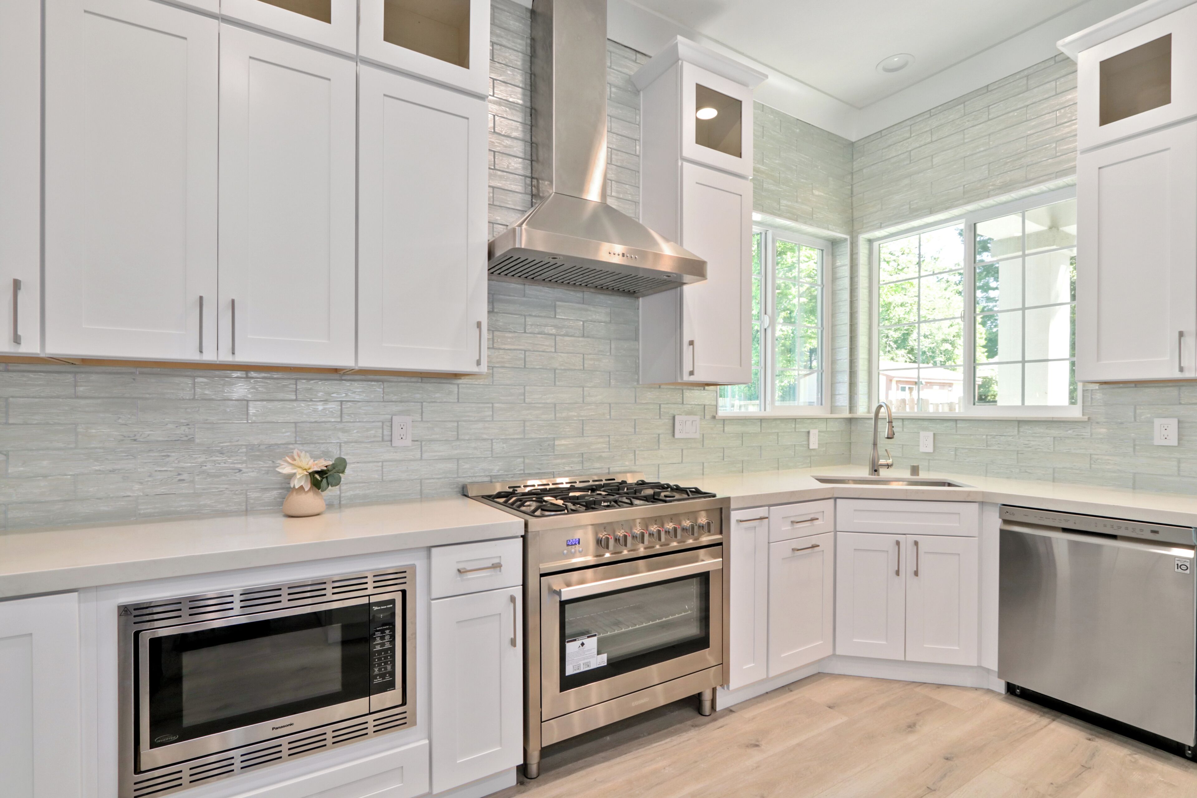 A modern kitchen with white cabinets, a stainless steel range, an oven, and a dishwasher.