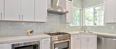 A modern kitchen with white cabinets, a stainless steel range, an oven, and a dishwasher.