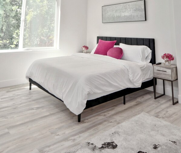 Un dormitorio moderno con estructura de cama de metal negro, ropa de cama blanca y una alfombra gris.
