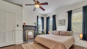 Un dormitorio con cama, ventilador de techo, chimenea y ventana con cortinas.