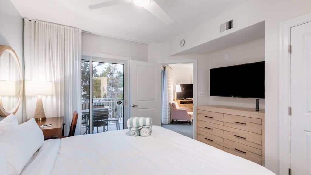 A hotel room with a bed, a TV, a desk, a chair, a dresser, and a balcony with a view.