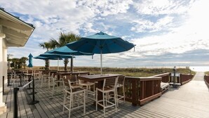 Een houten terras met buitenmeubilair, blauwe parasols en uitzicht op het strand.