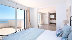 A bedroom with a large bed, a balcony with a view of the sea, and a bathroom with a mirror and sink.