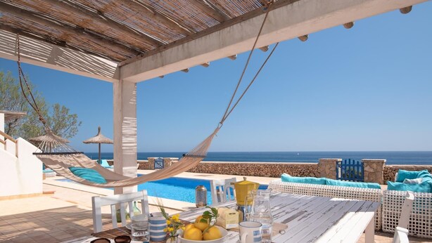 A poolside dining area with a table set for two, overlooking the sea.