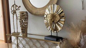 Una consola decorativa con un jarrón dorado, una escultura dorada y un espejo dorado.