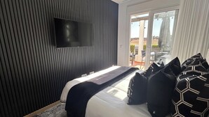 Una habitación de hotel moderna con una cama grande, un televisor de pantalla plana montado en la pared y vistas a un espacio exterior a través de una puerta de cristal.