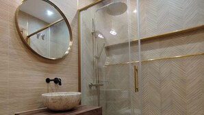 Un baño con un espejo redondo, un lavamanos de mármol y una ducha con paredes de vidrio.