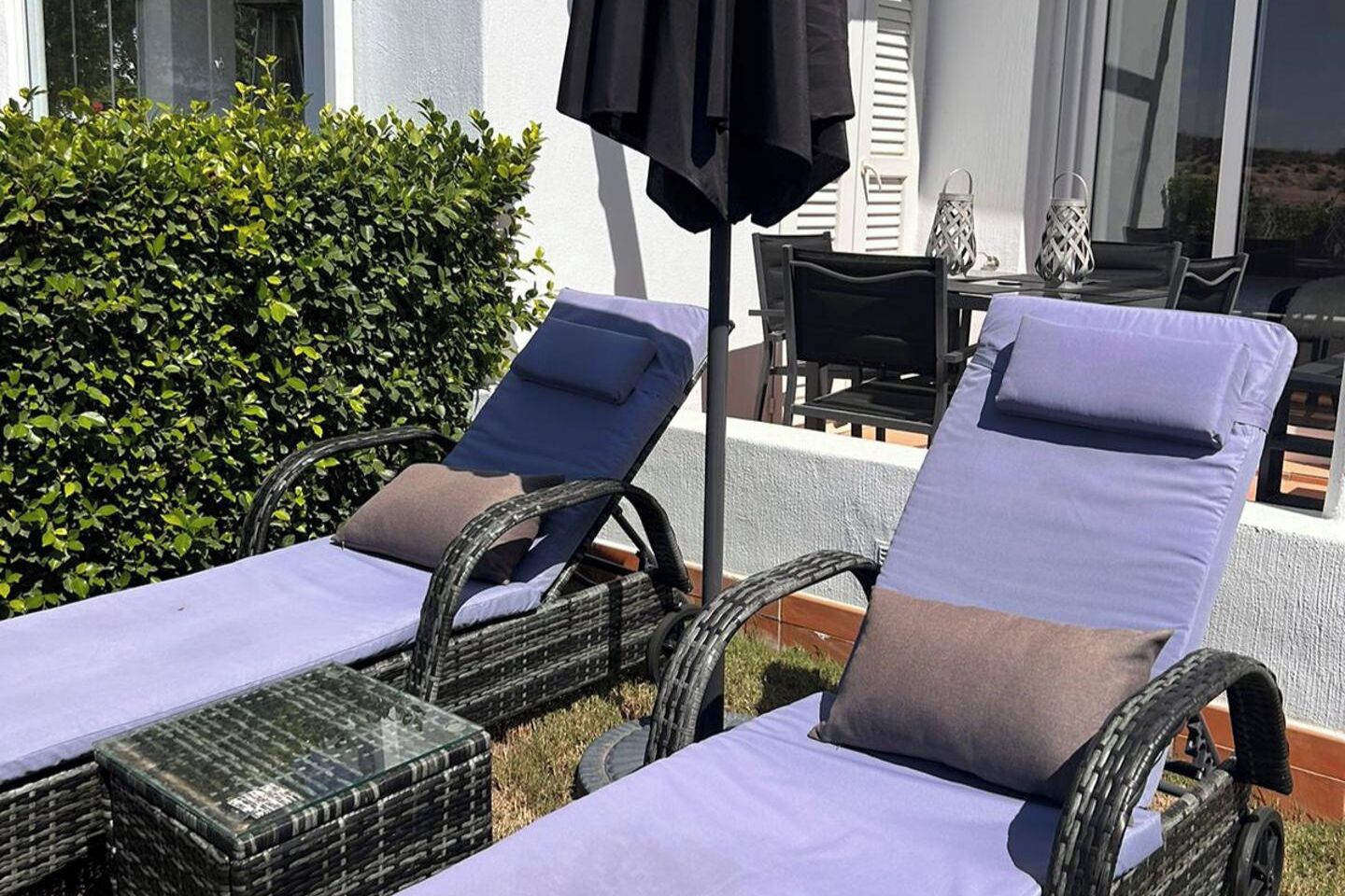 Two wicker lounge chairs with cushions, a table, and a black umbrella.