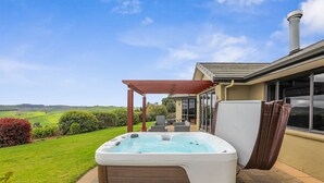 Un bain à remous dans un jardin, agrémenté d’une pergola, avec vue sur la campagne et une maison dotée de grandes fenêtres.
