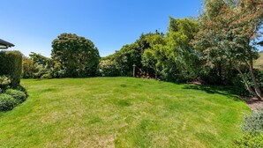 Une pelouse bien entretenue, agrémentée de divers arbres et arbustes, un ciel dégagé et un espace jardin bien visible.