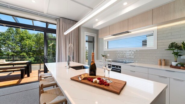 Una cocina moderna con una isla grande, un comedor con asientos exteriores y vistas a árboles.