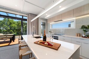 Una cocina moderna con una isla grande, un comedor con asientos exteriores y vistas a árboles.