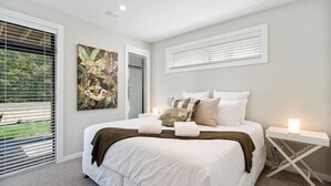 Un dormitorio con una cama grande, ropa de cama blanca, un cuadro y una mesita de noche con una lámpara.