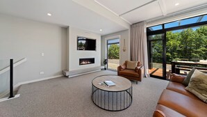 Un salón moderno con chimenea, una mesa de centro redonda, un sofá y un amplio ventanal con vistas al exterior.