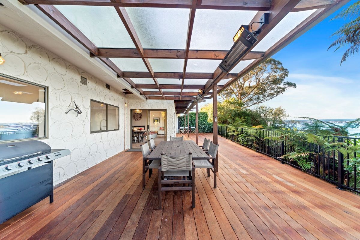Un patio exterior con terraza de madera, una parrilla y una mesa con sillas.