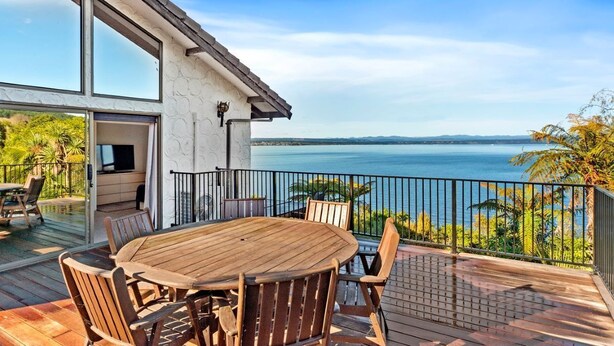 A wooden deck with a round table and chairs, overlooking a body of water.
