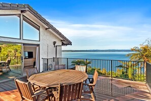 A wooden deck with a round table and chairs, overlooking a body of water. - All Decked Out on the Lake (Taupo)