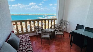 A balcony with a view of the sea, a sofa, and a table with chairs.