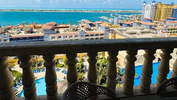 A balcony with a view of a coastal resort area, including a pool and various buildings.