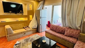 A modern living room with a flat-screen TV, a sofa, a coffee table, and a large window with curtains.