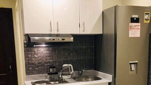A compact kitchen with white cabinets, a stainless steel refrigerator, and a black tiled backsplash.