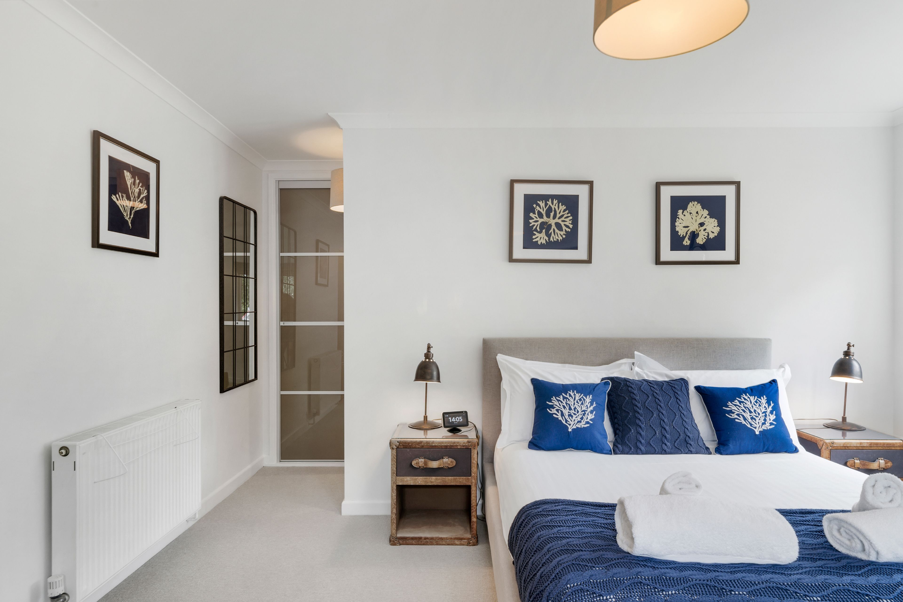 A bedroom with a bed, two nightstands, a radiator, and framed artwork on the walls.