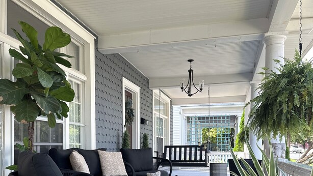 A covered porch with a black sofa, a wooden coffee table, and large potted plants. - Charming Pet-Friendly Stay: Walk BC, 7.5 mi to JMU, walk to Dining, Parks & more (Bridgewater)