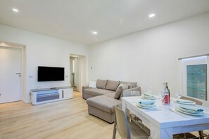 Un soggiorno moderno con una TV a schermo piatto, un divano, un tavolo da pranzo per due e una vetrina in vetro.