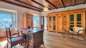 A spacious room with a wooden ceiling, a large wooden cabinet with glass doors, a dining table with chairs, and a wicker chair. - Appartamento Sole: Lake Maggiore Lakefront and Panoramic View, Sesto Calende, Italy (Sesto Calende)