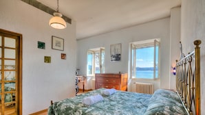 A bedroom with a bed, a dresser, a radiator, and a window with a view. - Appartamento Sole: Lake Maggiore Lakefront and Panoramic View, Sesto Calende, Italy (Sesto Calende)