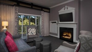 Une chambre d’hôtel avec une cheminée, un canapé, un fauteuil et une télévision.