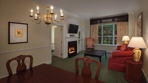 A hotel room with a fireplace, a television, a red sofa, a dining table, and a chandelier.