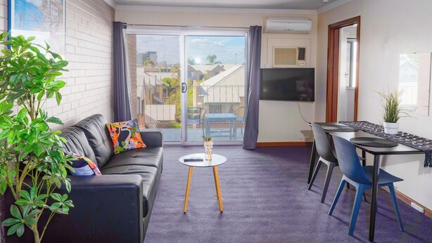 A modern living room with a sofa, a small round table, and a dining area with chairs. - Spacious & Cosy self-contained 1 bedroom apartment
 (Rivervale)