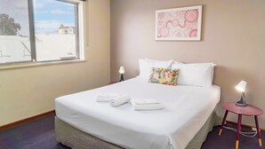 A hotel room with a bed, a window, a bedside table with a lamp, and a wall-mounted artwork. - Spacious & Cosy self-contained 1 bedroom apartment
 (Rivervale)