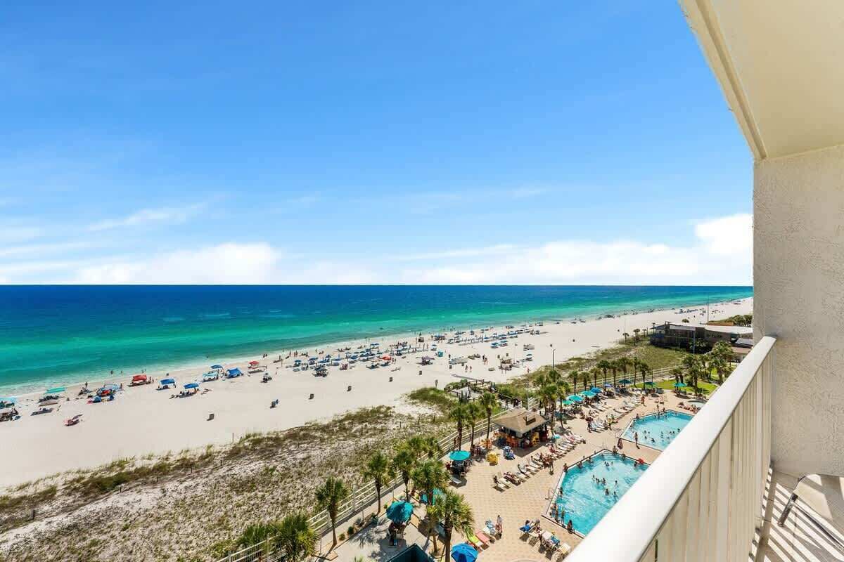 A beach resort with a pool area, beach chairs, umbrellas, and a view of the ocean.