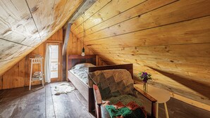 Une chambre mansardée chaleureuse avec un plafond en pente en bois, un lit simple, une chaise, une petite table et une fenêtre.