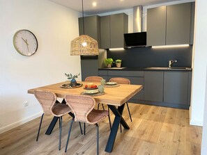 Ett modernt kök med grå skåp, en svart TV och en matplats med ett träbord och stolar av rotting.