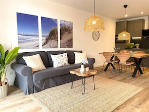 En moderne stue med sofa, sofabord, spisebord, fletstole og et ur på væggen.