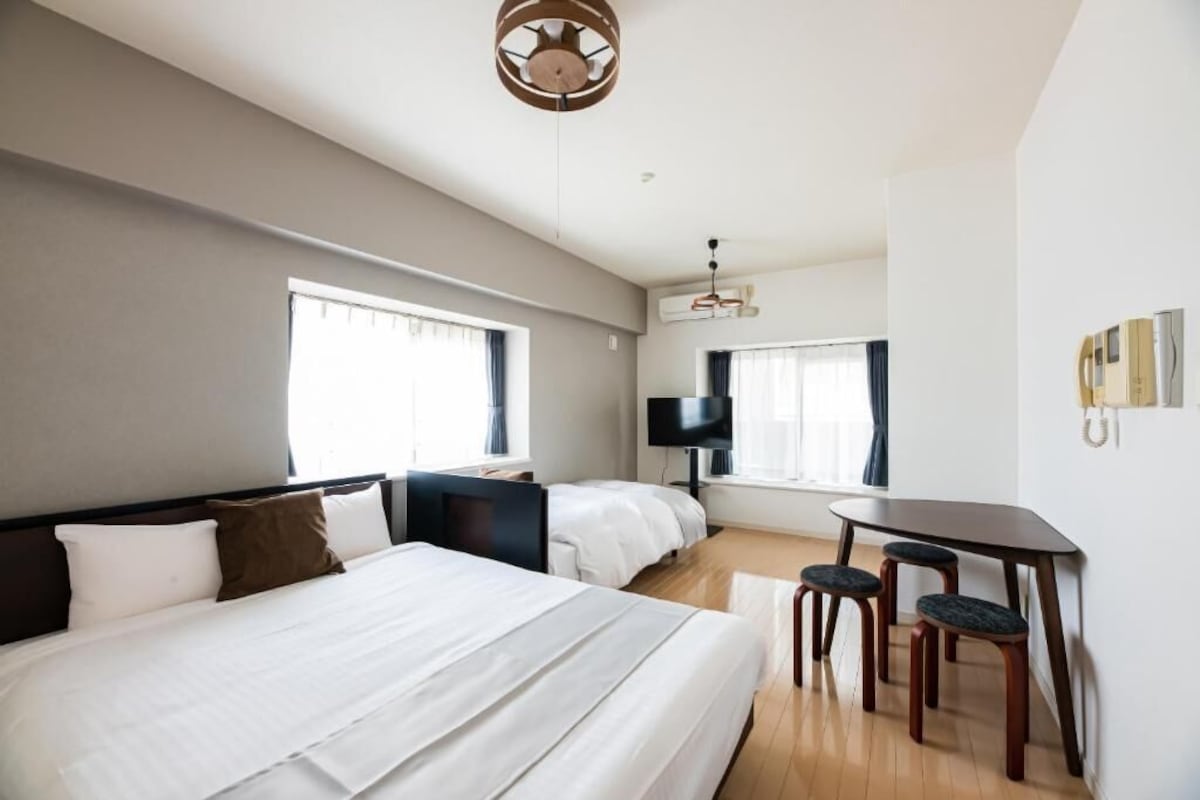 Una habitación de hotel con una cama grande, un escritorio con dos sillas, un televisor y una ventana.
