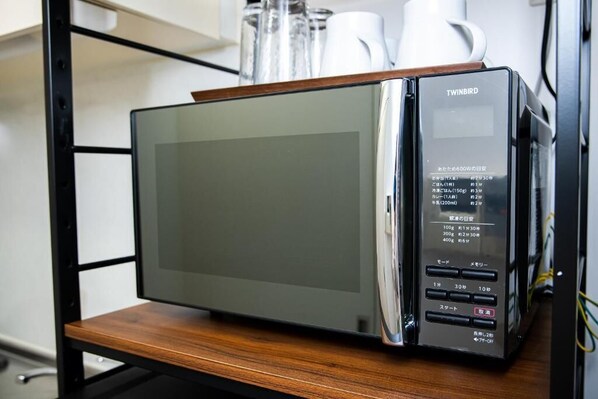 Forno de micro-ondas com visor digital e painel de controle, sobre uma prateleira de madeira.