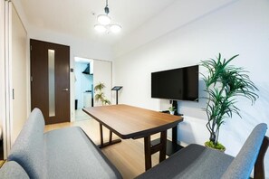 A modern living room with a sofa, a wooden table, a flat-screen TV mounted on the wall, and a potted plant.