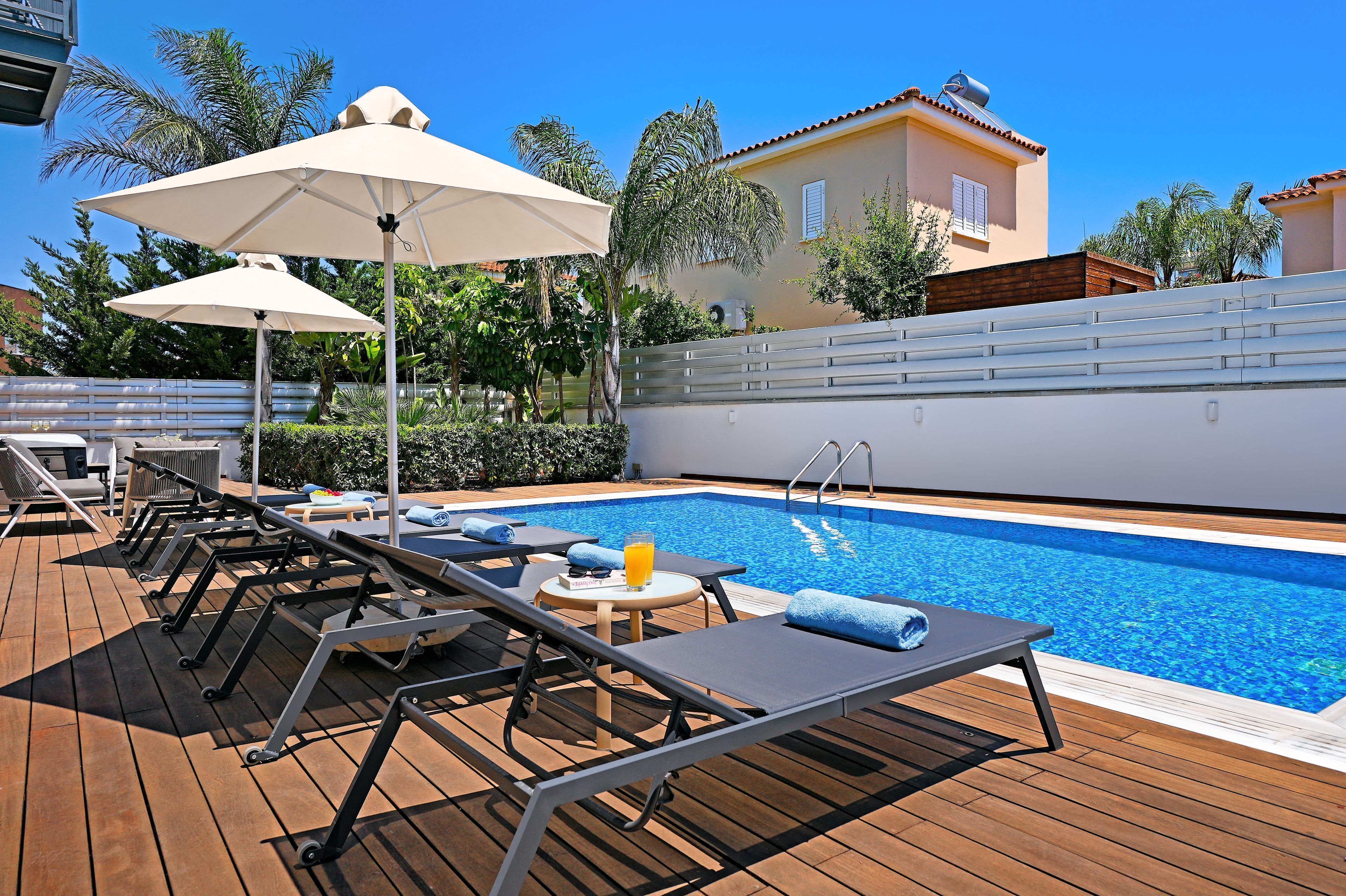 Zona de piscina con sillas de descanso, sombrillas y una mesa pequeña con una bebida.