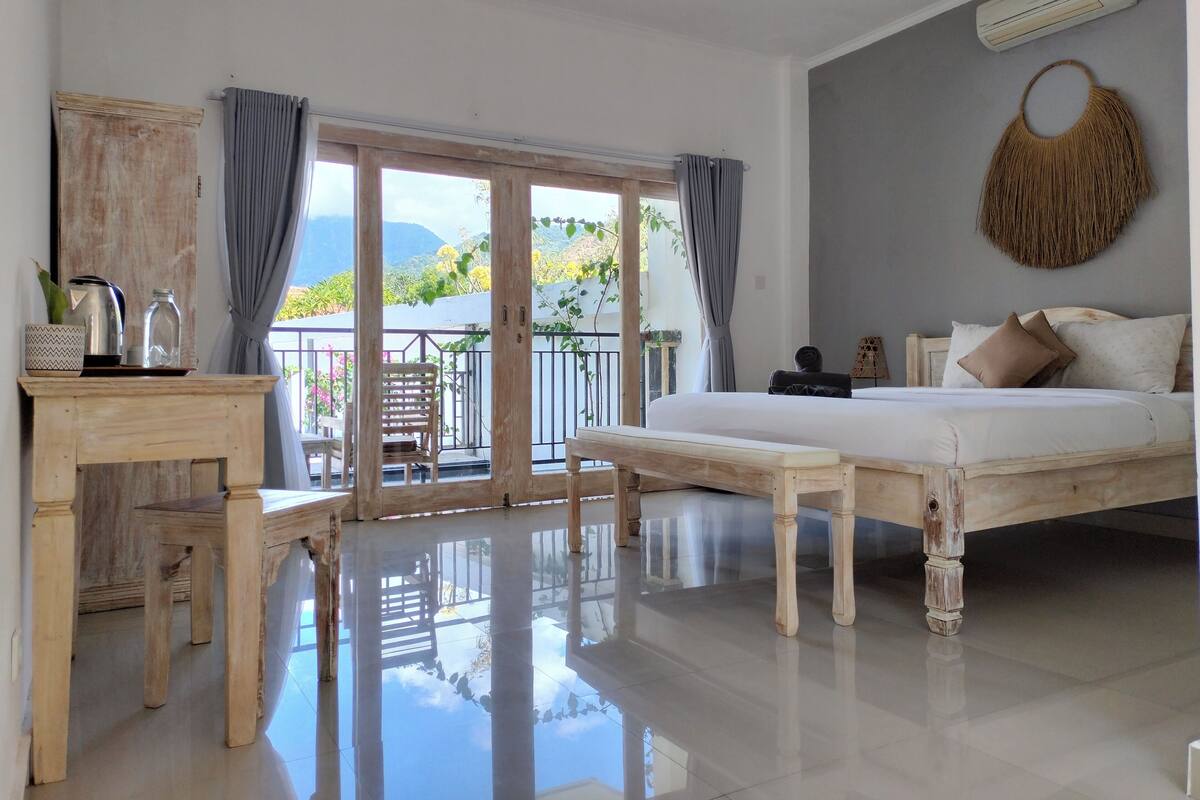 Un dormitorio con cama, escritorio de madera, silla y balcón con vistas al exterior.
