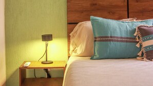 Un dormitorio con cabecera de madera, cama con ropa de cama blanca, almohada azul y mesita de noche con lámpara.
