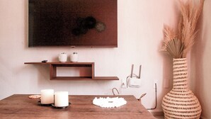 Una mesa de madera para comer con velas, un mantel individual blanco y un jarrón tejido con plantas secas.