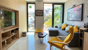 A modern living room with a flat-screen TV, a sofa, a yellow armchair, and a coffee table. - Stunning sunset view from the rooftop infinity pool. 5 min walk to the beach. (Puerto Vallarta)