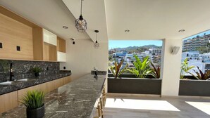 A modern kitchen with a marble countertop, wooden cabinets, and a view of a cityscape. - Stunning sunset view from the rooftop infinity pool. 5 min walk to the beach. (Puerto Vallarta)