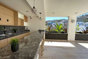 A modern kitchen with a marble countertop, wooden cabinets, and a view of a cityscape.