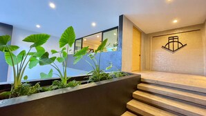 A modern interior with a staircase leading to a second floor, a concrete planter with greenery, and a wall-mounted logo. - Stunning sunset view from the rooftop infinity pool. 5 min walk to the beach. (Puerto Vallarta)